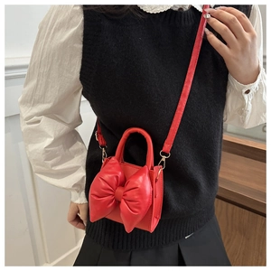 Detail of red PU leather handbag featuring a large bow accent and adjustable crossbody strap