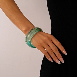 Close-up of a wide geometric acrylic bangle with green and brown ink-wash textures