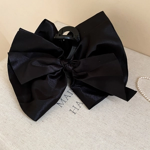 Close-up of a large black satin bow hair claw clip with silk texture on beige display