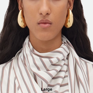 Close-up of large polished gold teardrop earrings worn by a model for a stylish metal look