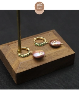 Detail of baroque pearl earrings with gold metal rings and green gemstone accents