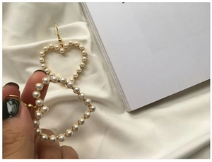 Close-up of hand holding a gold heart-shaped hoop earring with inlaid white pearls
