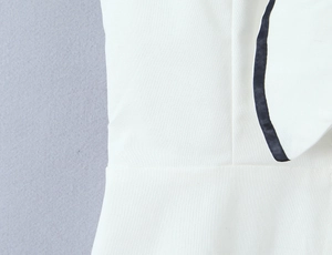 Detail of white linen dress featuring contrast black satin piping and fine stitching