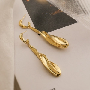 Macro shot of gold twisted flowing earrings on artistic background with glass