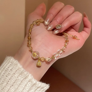 Detail view of crystal beaded bracelet with golden lotus bell pendant on woman wrist