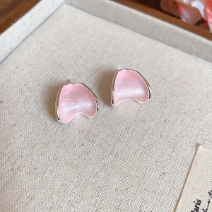 Macro shot of pink petal-shaped stud earrings with silver edges on beige fabric