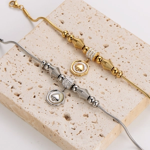 Snake chain bracelets in gold and silver with heart pendants on travertine stone