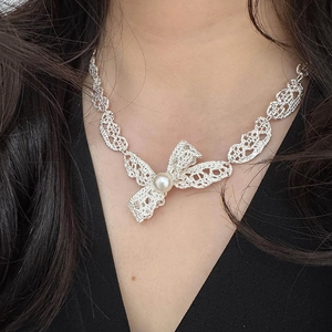 Élégant collier pendentif nœud argenté avec perle centrale porté par une femme