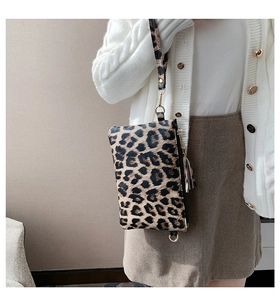 Detail of leopard print envelope clutch with gold tassel and wrist strap held by model
