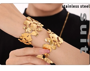 Detail of a bold gold stainless steel flower cuff bracelet worn on a model's wrist