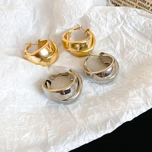 Close-up of chunky gold and silver double-layered hoop earrings on white textured background