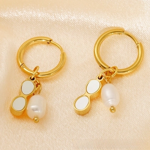 Detailed close-up of gold hoop earrings with white enamel charms and pearls on silk fabric
