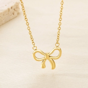 Macro shot of gold bow tie pendant necklace with polished metallic finish on textured paper