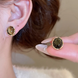 Detail showing vintage gold-rimmed tiger eye stone stud earring on a model