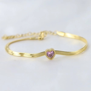 Macro view of a 14K gold-plated snake chain bracelet with a pink heart-shaped crystal
