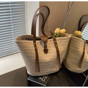 Detail of beige straw tote bag with brown leather straps and metal buckle accent