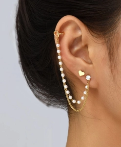 Detail of gold heart earrings with pearl tassels and ear cuff on a model's ear