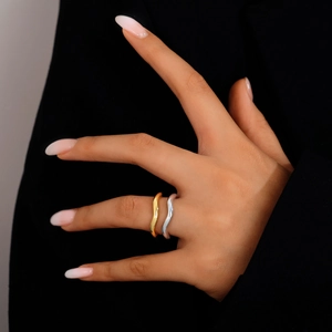Detailed view of gold and silver wave-shaped rings on hands over dark fabric