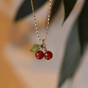 Elegant gold necklace featuring red cherry pendants with green leaves in a soft natural setting