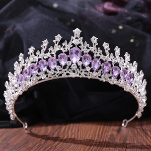 Detailed view of silver crown with teardrop purple crystals and rhinestones on dark wood