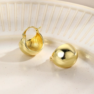 Close-up of polished gold teardrop huggie earrings on a beige textured ceramic tray
