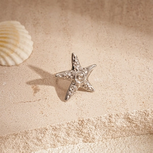 Detailed view of a silver starfish ear clip on a stone surface with a seashell background