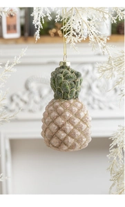 Close-up of pink and green glitter pineapple ornament hanging on a white festive branch