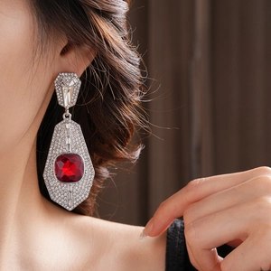 Close-up of geometric silver earring with large red gemstone and crystal pave detailing