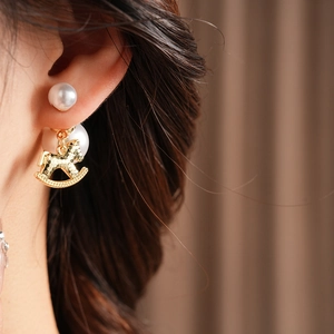 Macro view of gold rocking horse pearl earring worn by model on a dark background