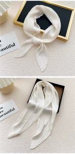 Detailed close-up of white pleated silk scarf tied on elegant beige textured backdrop