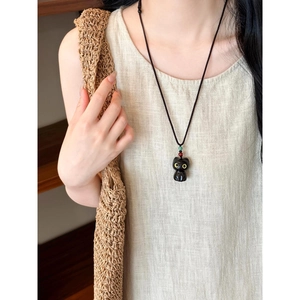 Gros plan du collier pendentif chat noir porté par un modèle dans un style naturel