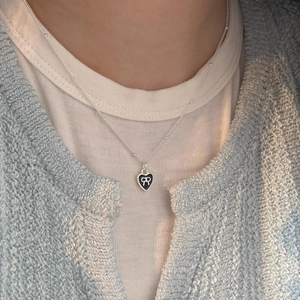 Close-up of black heart enamel pendant with white bow logo on a silver bead chain