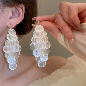 Detail of silver needle geometric shell tassel earrings worn by a model on vacation