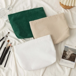 Three corduroy cosmetic bags in green, beige and white on a natural soft fabric background