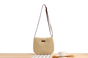 Detail of hand-woven straw crossbody bag with brown leather patch and adjustable strap