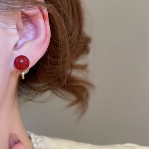 Close-up of elegant red spherical clip-on earring with gold-tone hardware on ear