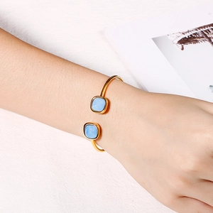 Detailed view of model wearing a gold open bangle with square blue gemstones