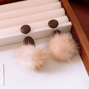 Close-up of winter earrings featuring brown wooden disks and soft beige faux fur pom poms