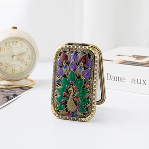 Detail of vintage peacock embossed metal makeup mirror with colorful enamel inlays