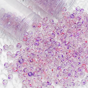 Macro detail of 8mm purple and red speckled glass beads for DIY jewelry on white fur