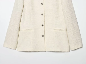 Detail van crème wit tweed jasje met donkere metalen knopen en functionele zakken