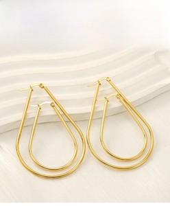 Detail of oversized gold teardrop earrings on a minimalist white textured backdrop