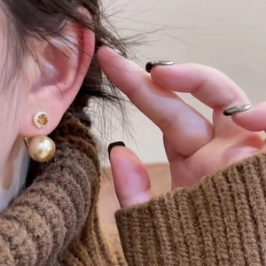 Detail of golden pearl earrings with crystal flower studs worn by a model in warm light