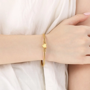 Bracelet jonc ouvert en fil d'acier doré avec cœur pour femme porté par un modèle