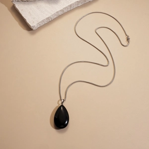 Detail of a polished black teardrop stone pendant on a silver chain necklace