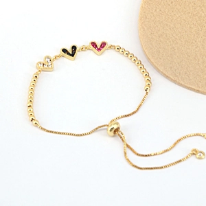 Detail of gold adjustable chain bracelet featuring white, black and pink heart-shaped stones