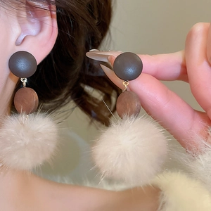 Detail of wooden geometric stud with cream pompom drop shown on model's ear