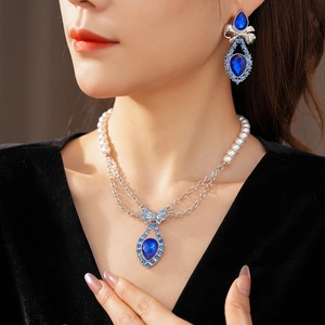 Detail of silver bow jewelry set with blue teardrop stones and pearl chain necklace