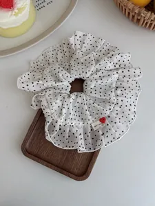 Detail of white polka dot scrunchie with red heart button and handmade label on wood tray