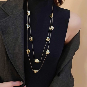 Dettaglio della collana dorata multistrato geometrica indossata su un maglione scuro